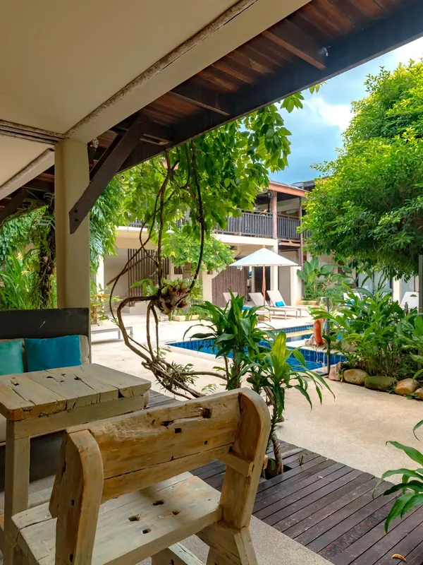 Terrasse ombragée avec tables en bois et piscine au fond