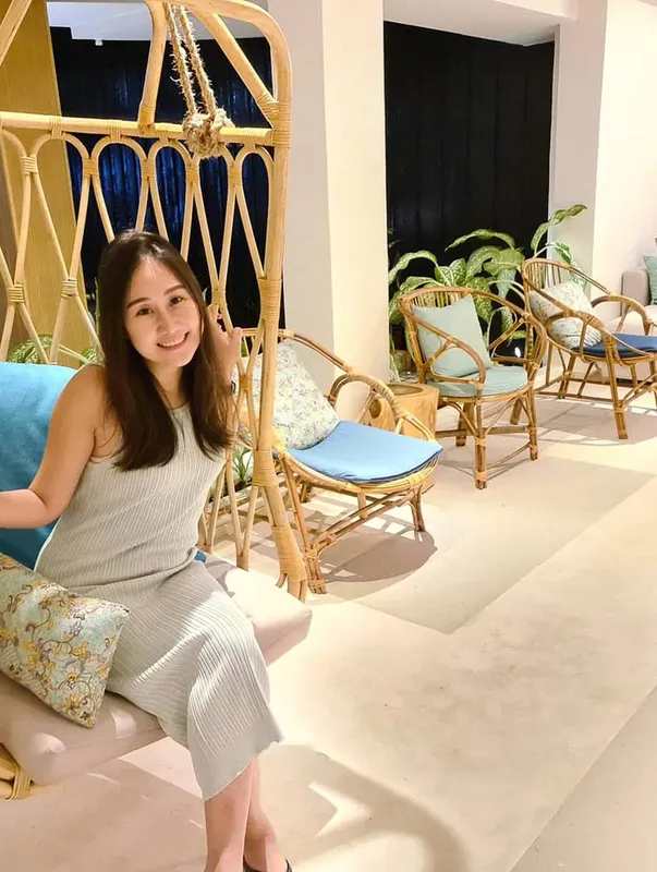 Jeune femme souriante assise dans un fauteuil suspendu en rotin