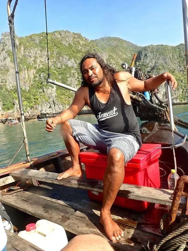 Homme souriant assis sur un bateau en bois au large d'une côte