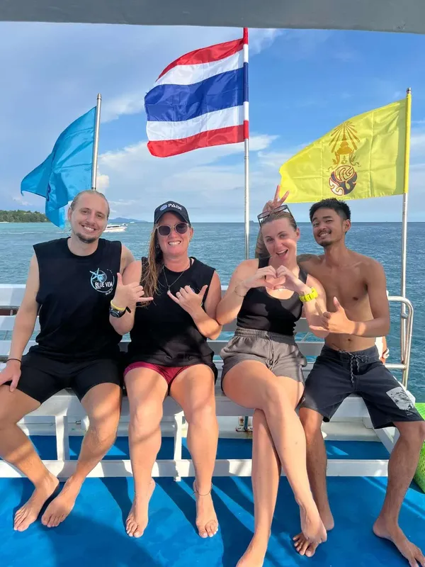 Quatre personnes souriantes sur un bateau en mer, drapeau thaïlandais