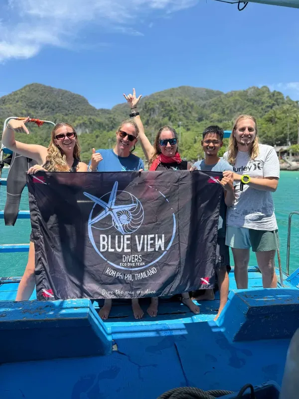 Groupe de plongeurs souriants tenant une bannière devant un bateau