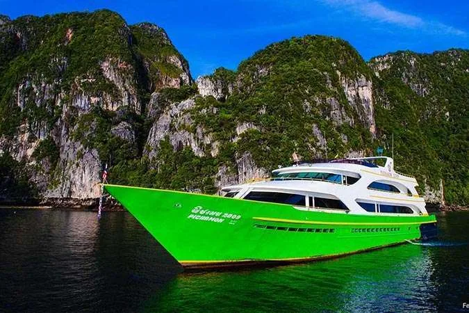 Grand bateau de plongée vert et blanc navigue devant des falaises