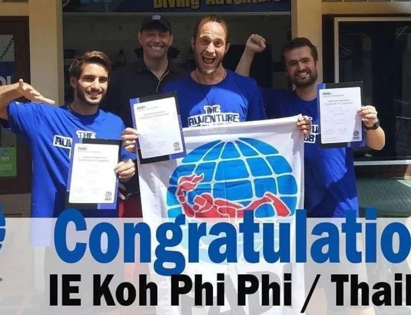 Quatre plongeurs souriants présentent leurs certificats PADI devant un centre
