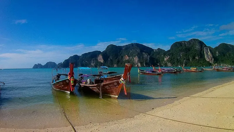 Plage de sable fin avec bateaux traditionnels et montagnes verdoyantes