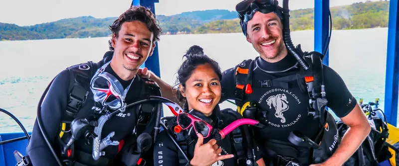 Trois plongeurs souriants équipés sur un bateau en mer