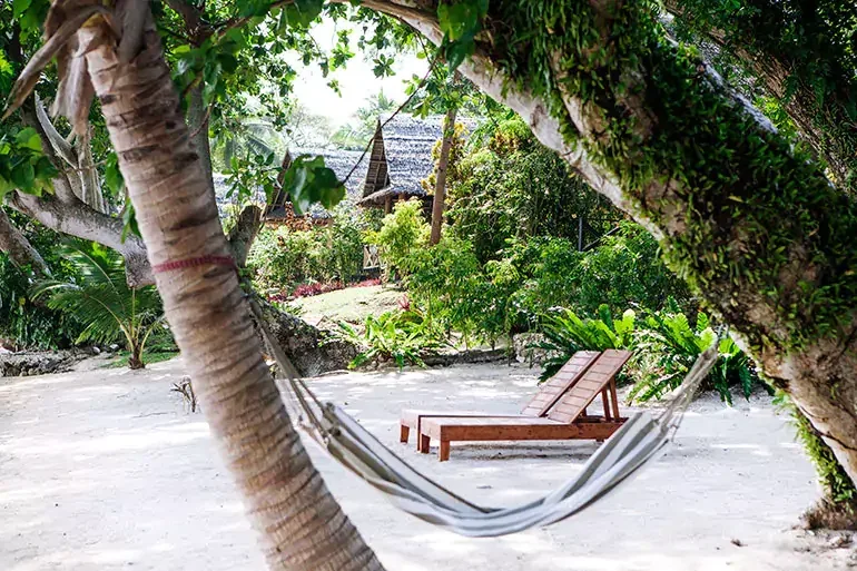 Hamac suspendu entre deux arbres, transats sur plage de sable blanc