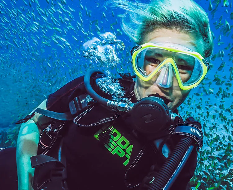 Plongeuse souriante entourée de petits poissons dans l'eau bleue