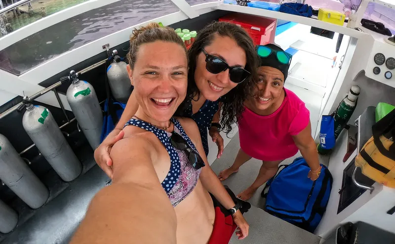 Trois femmes souriantes sur un bateau de plongée avec équipement