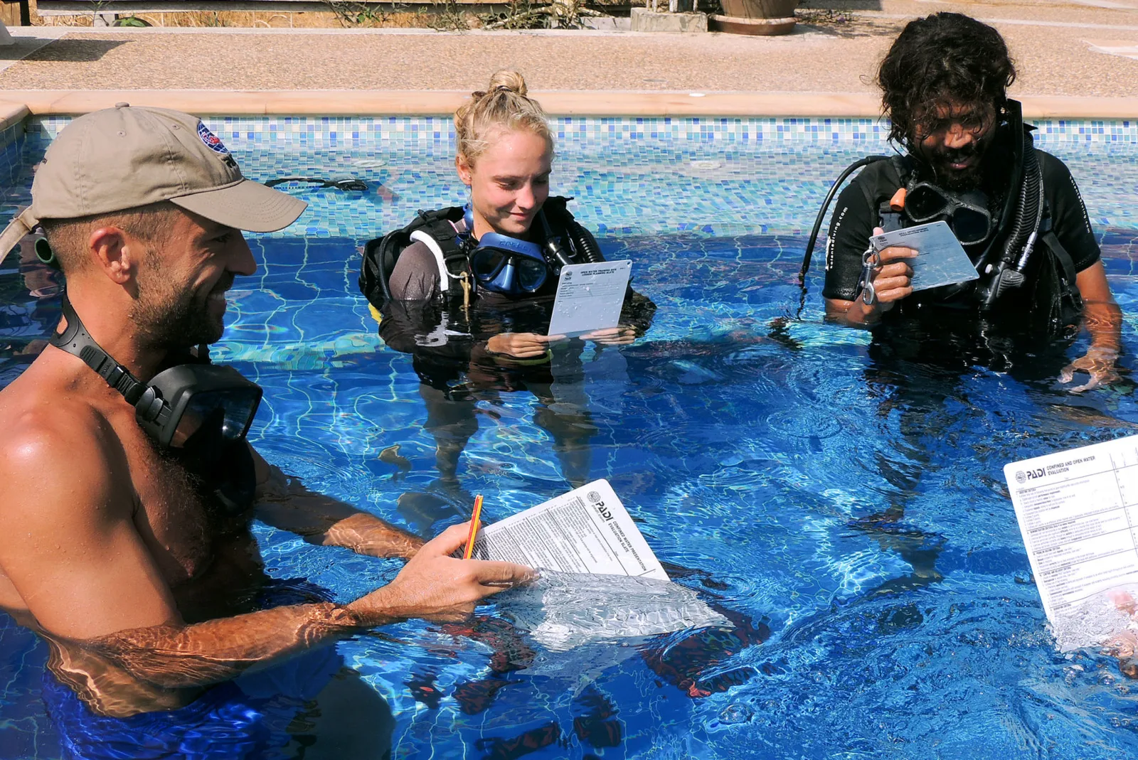 Trois personnes en combinaison de plongée dans une piscine avec des ardoises