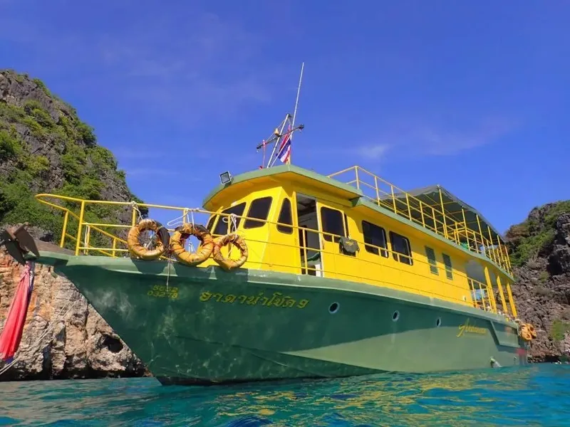 Bateau jaune et vert amarré près d'îles rocheuses sous ciel bleu