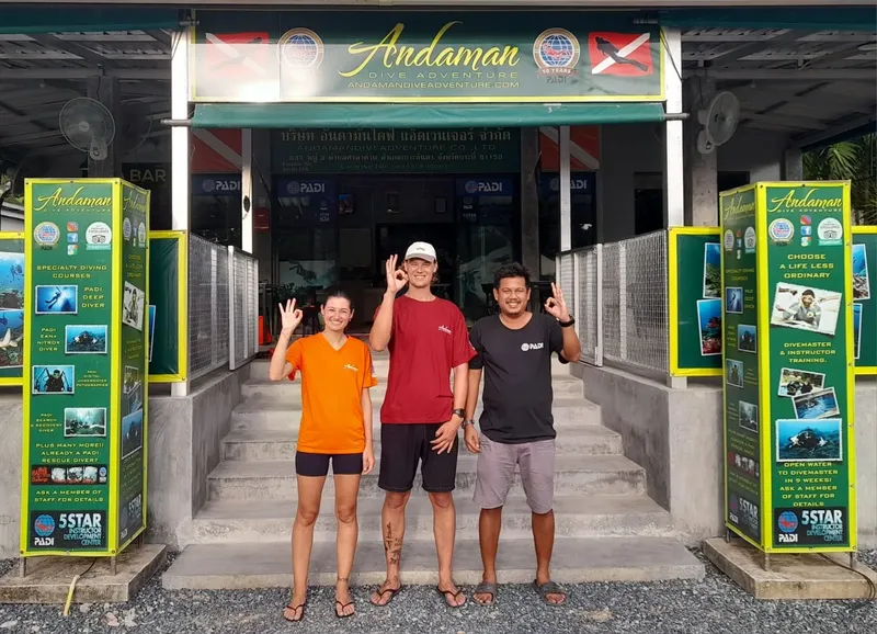 Trois personnes souriantes devant l'entrée d'un centre de plongée PADI