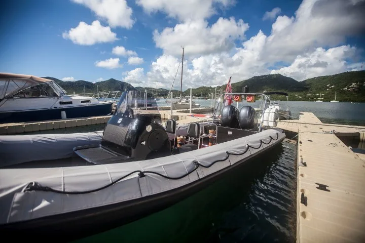 Bateau semi-rigide amarré à un ponton ensoleillé avec des bateaux en arrière-plan