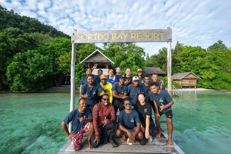 Groupe de personnes souriantes posant devant un resort tropical en bois