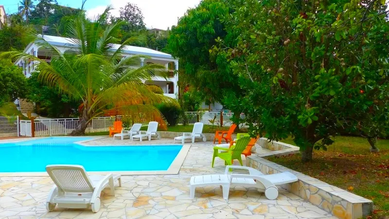 Piscine et transats devant un bâtiment blanc entouré de végétation tropicale