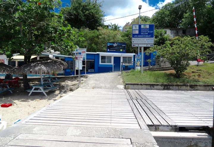 Centre de plongée avec bâtiments bleus, plage et accès au ponton