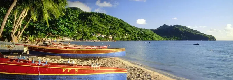 Bateaux colorés amarrés devant une côte montagneuse et une mer bleue