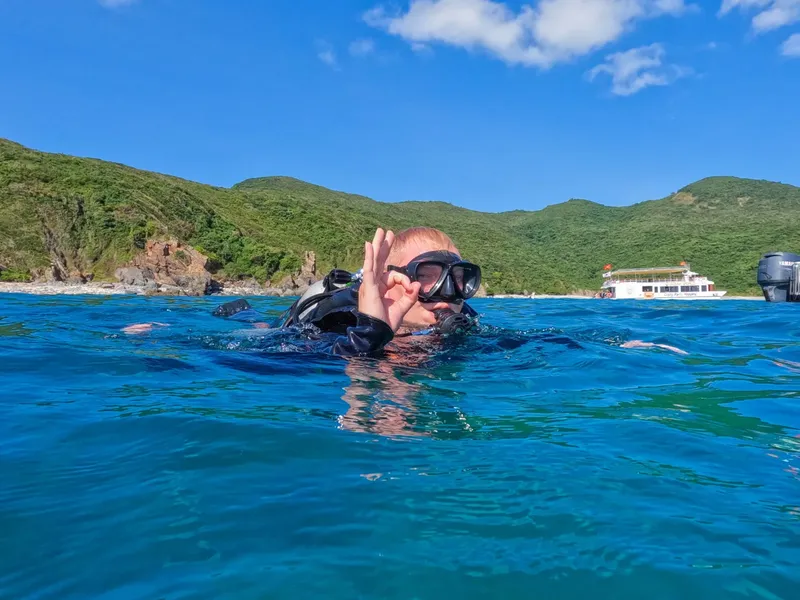 Plongeur avec masque et combinaison, nageant en mer turquoise, paysage côtier