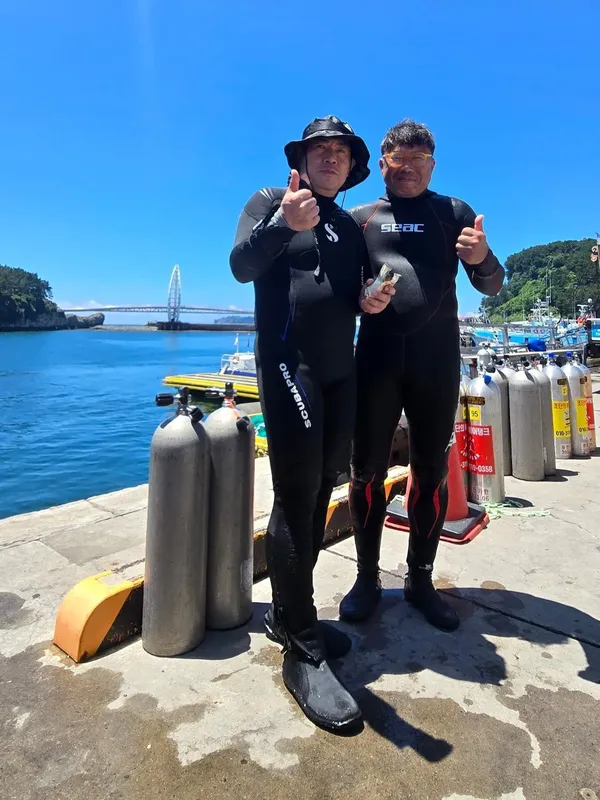 Deux plongeurs équipés sourient sur un quai ensoleillé