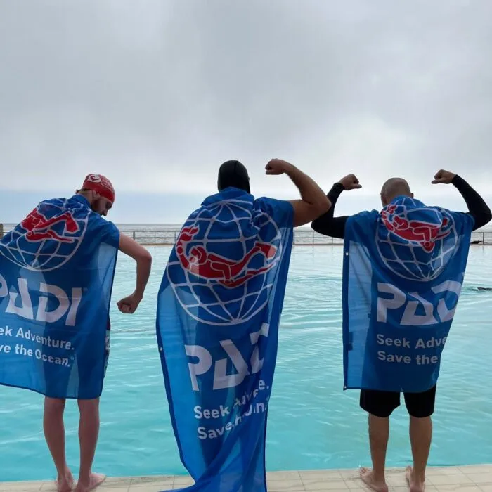 Trois personnes portent des peignoirs PADI bleu au bord d'une piscine