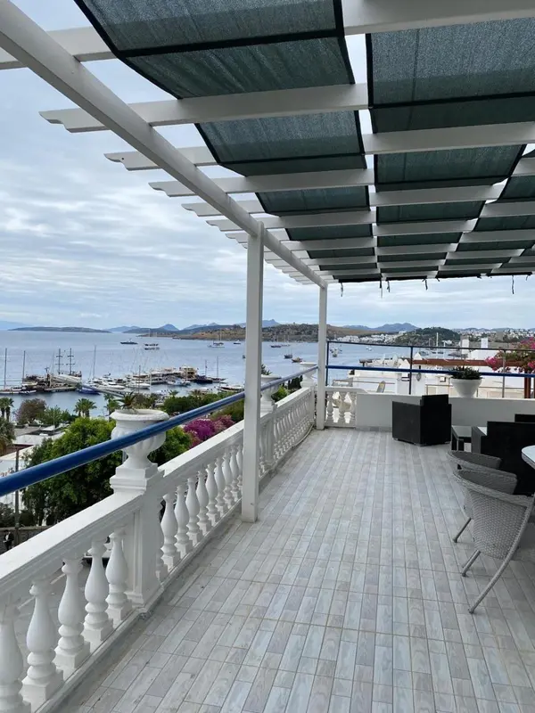 Terrasse ombragée avec vue sur un port de plaisance et la mer.