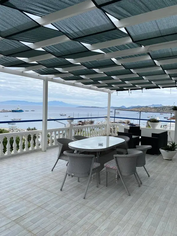 Terrasse ombragée avec table et chaises donnant sur la mer.