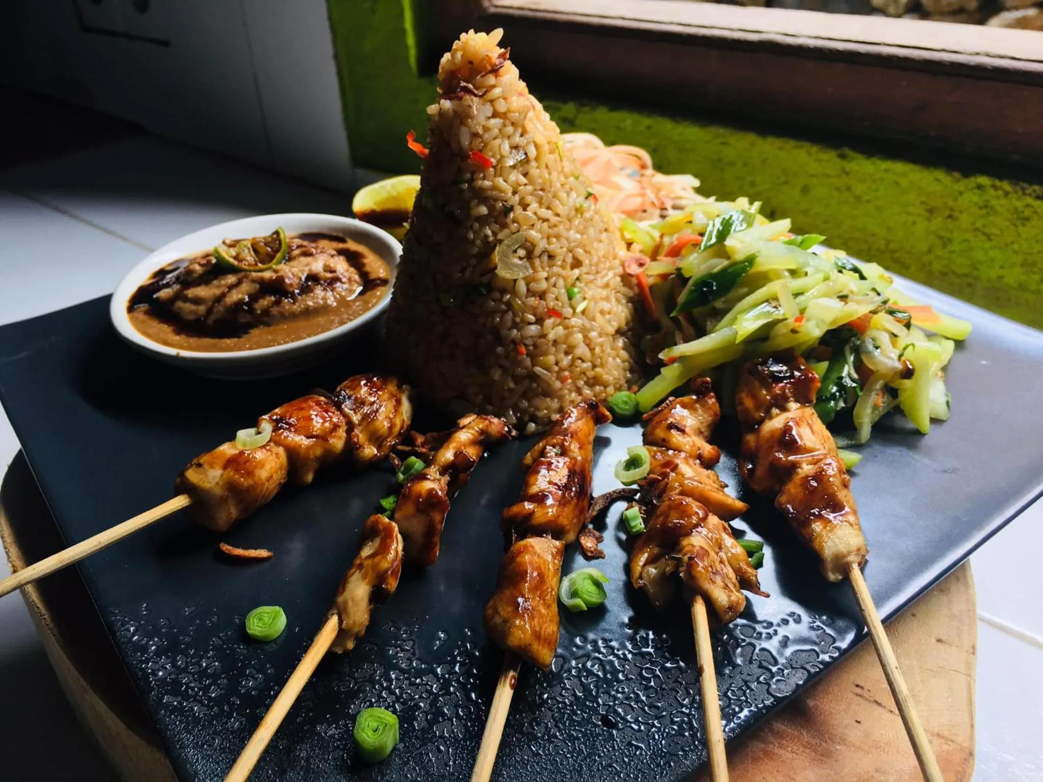 Assiette de riz frit en forme de cône, accompagnée de brochettes de poulet et d'une sauce.