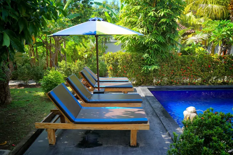 Transats bleus et bois alignés au bord d'une piscine turquoise dans un jardin luxuriant.