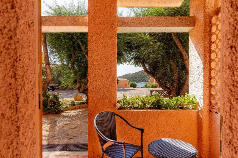 Une terrasse ombragée donne sur un jardin et la mer au loin.