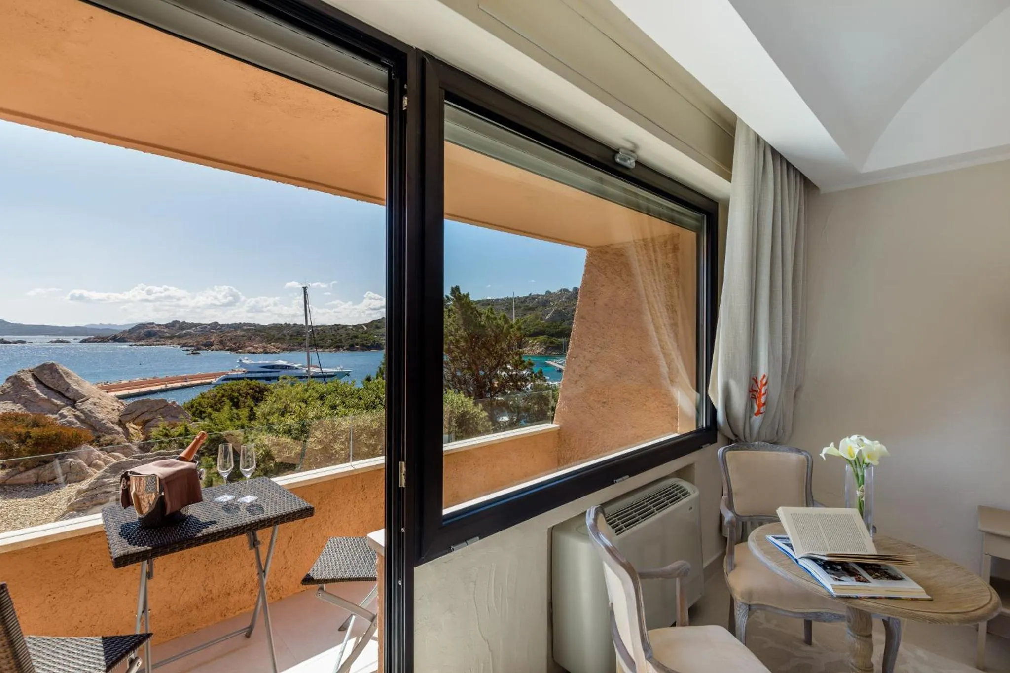 Une petite table avec des verres et une bouteille est posée sur un balcon avec vue sur la mer.