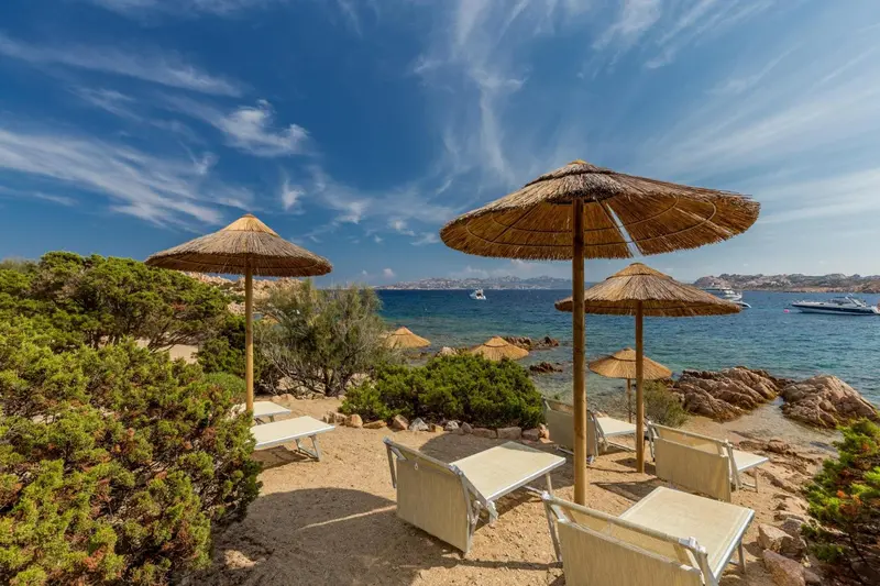 Transats et parasols de plage sur un rivage rocheux ensoleillé.