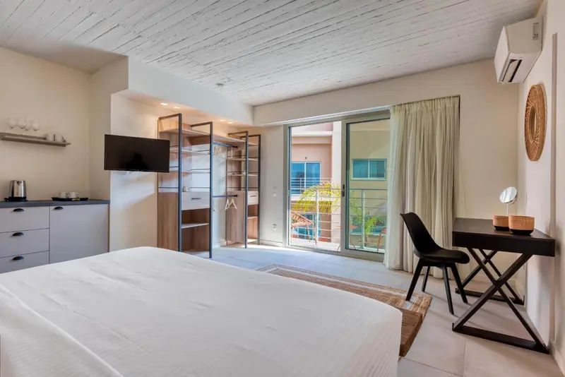 Une chambre lumineuse avec un lit blanc et un bureau près d'une baie vitrée.