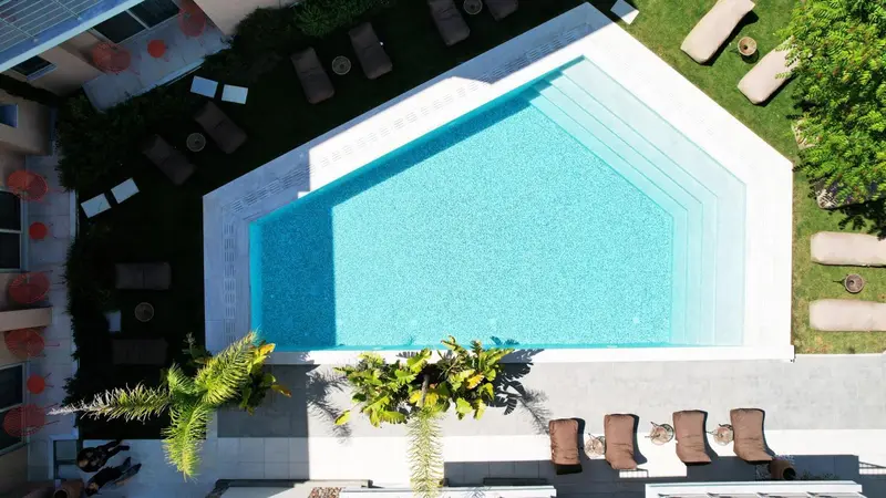Vue aérienne d'une piscine rectangulaire entourée de transats et de végétation.