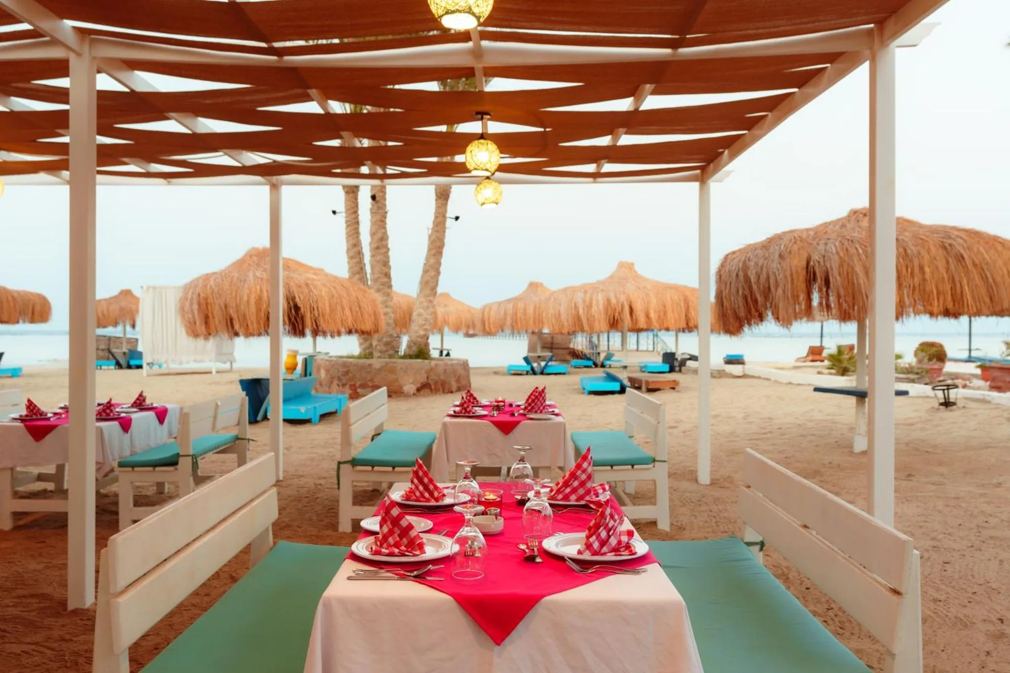 Tables dressées sur une terrasse en bord de mer avec des parasols en chaume.