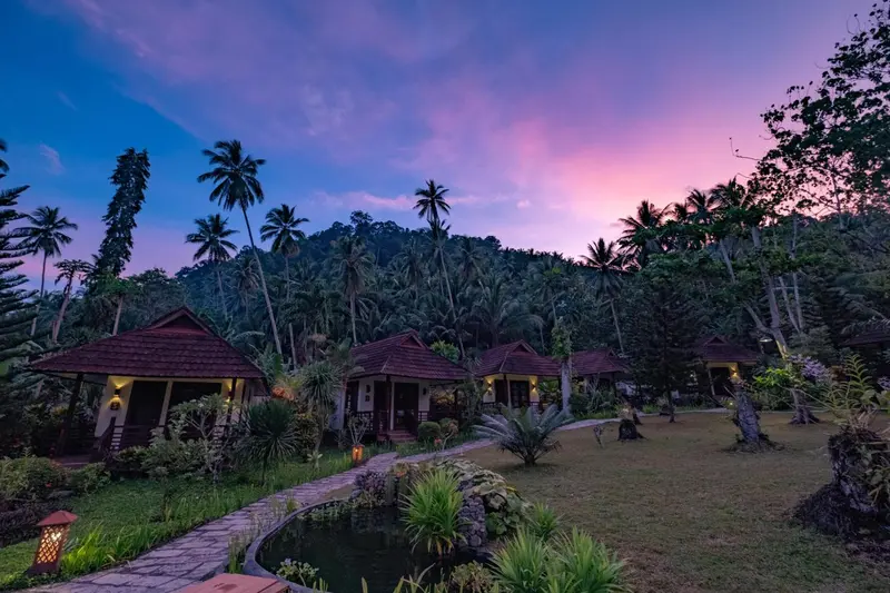 Petites maisons de vacances au toit de chaume dans un jardin tropical au crépuscule.