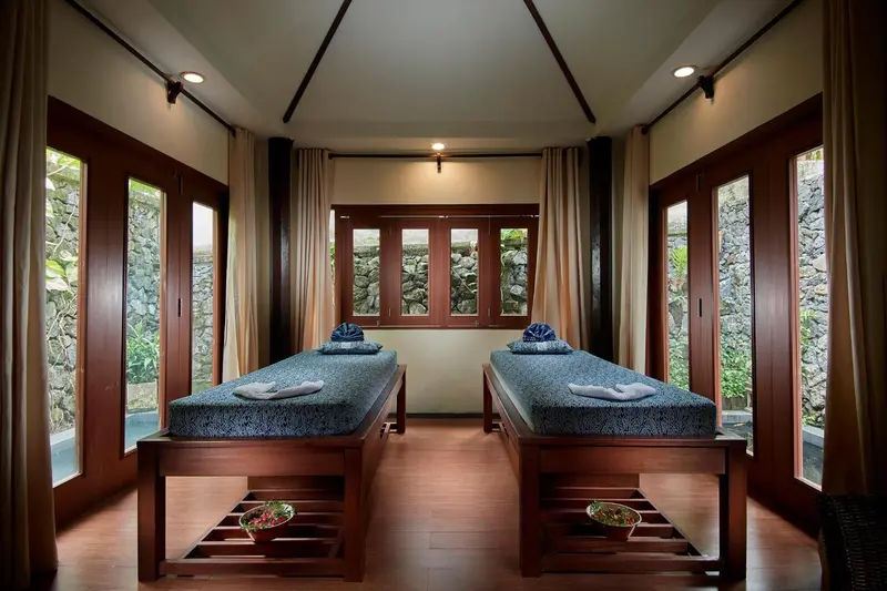 Deux tables de massage sont disposées dans une pièce lumineuse avec de grandes fenêtres.