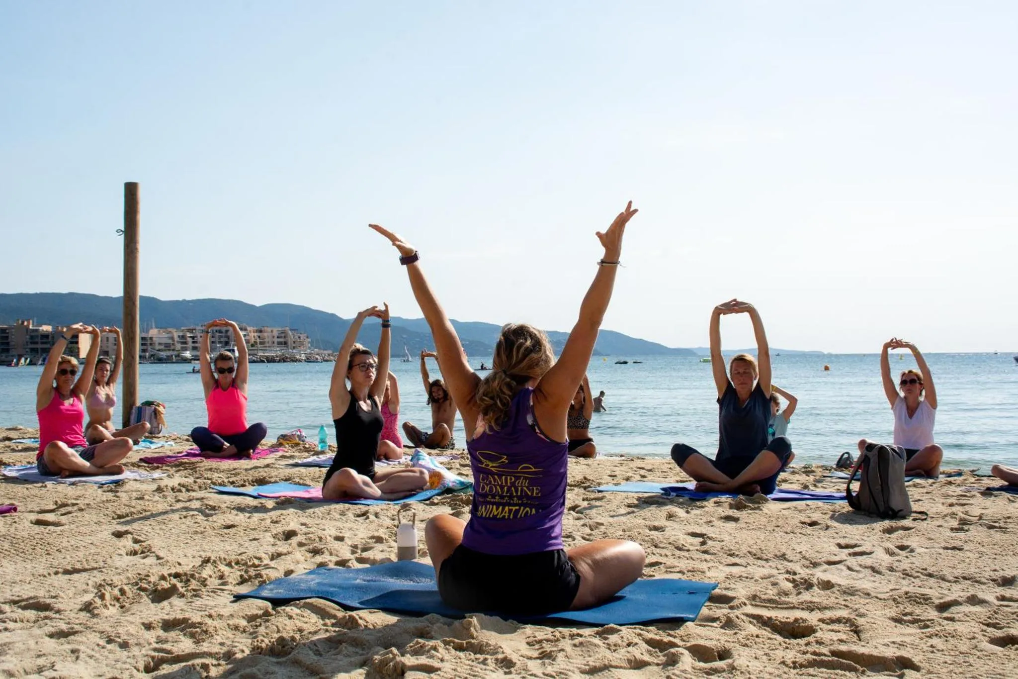 Groupe de personnes pratiquant le yoga sur une plage de sable fin face à la mer.
