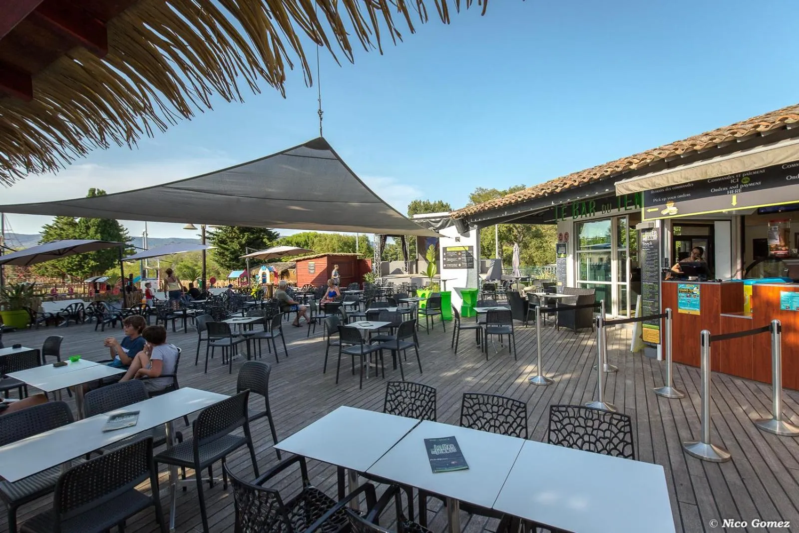 Terrasse ombragée avec tables et chaises près d'un comptoir de service.