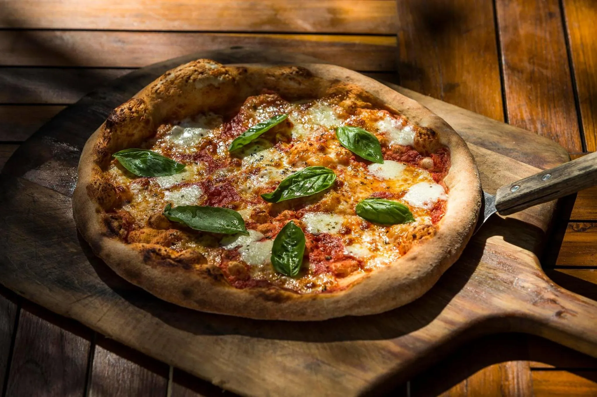Une pizza margherita fraîchement cuite est présentée sur une planche à pizza en bois.