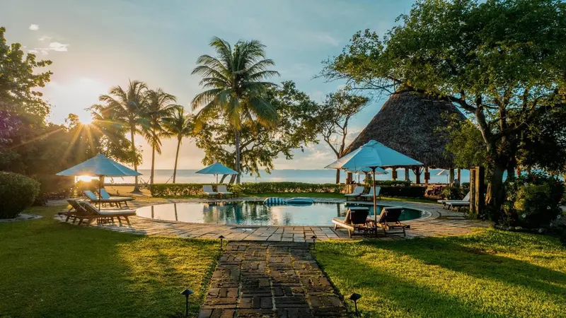 Une piscine bordée de chaises longues et de végétation luxuriante au coucher du soleil.
