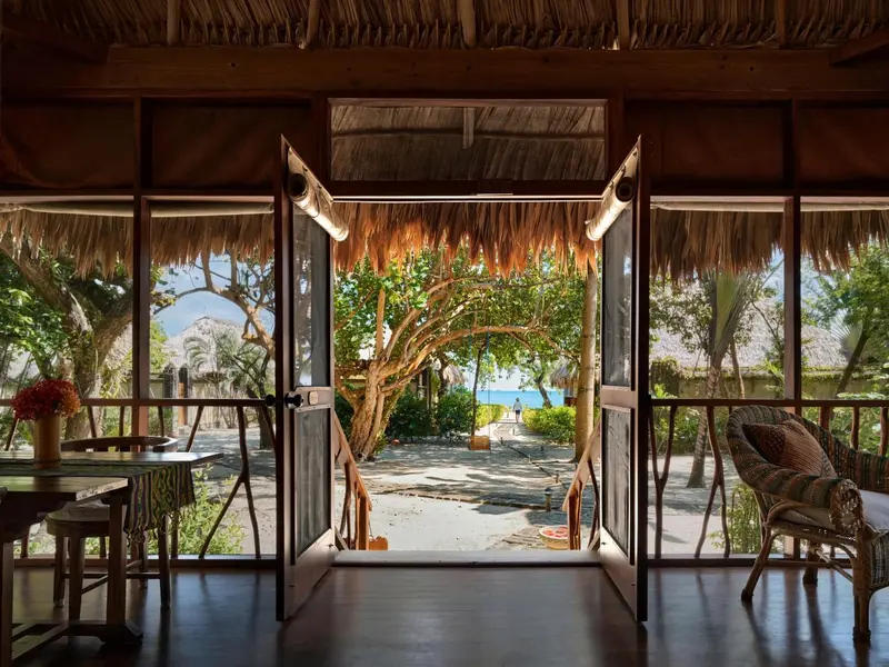 Une terrasse en bois s'ouvre sur une végétation luxuriante et une plage.