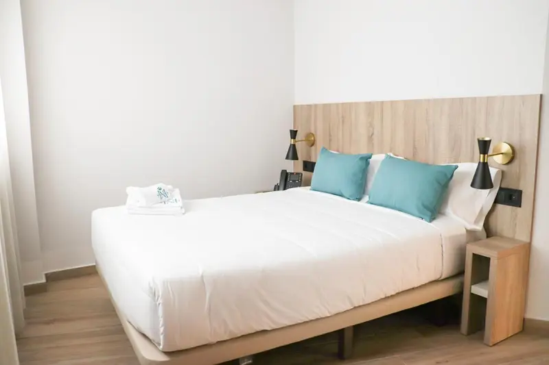 Une chambre lumineuse avec un grand lit et des oreillers turquoise.
