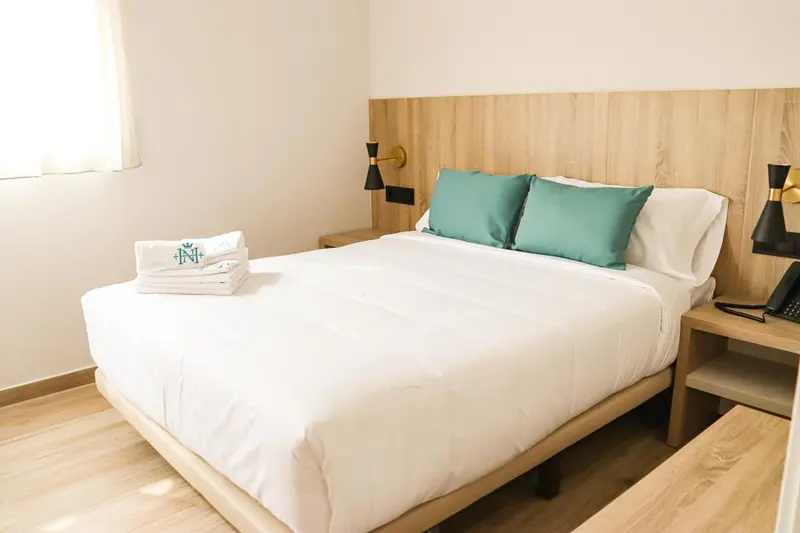 Lit double avec oreillers verts dans une chambre lumineuse.