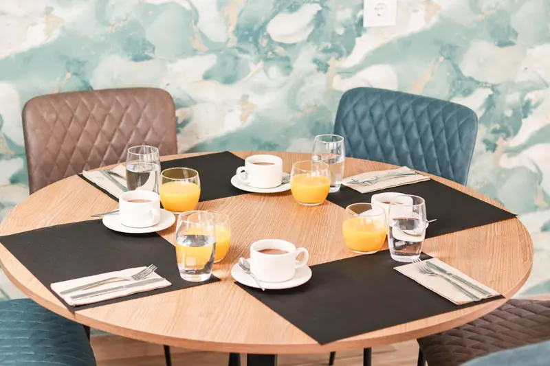 Une table ronde est dressée pour le petit-déjeuner avec des couverts, des verres et des boissons.