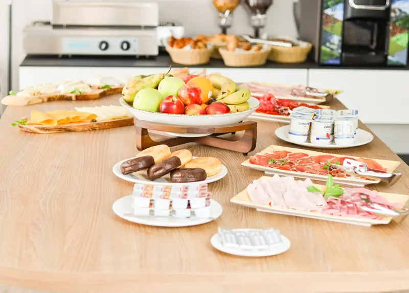 Une table garnie de viennoiseries, de fruits et de charcuteries.