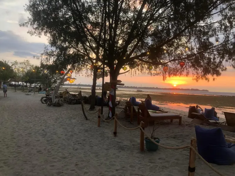 Des transats bleus sont disposés sur une plage de sable au coucher du soleil.
