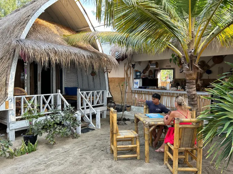 Une terrasse ombragée avec des tables et des chaises en bambou, face à un comptoir de bar.