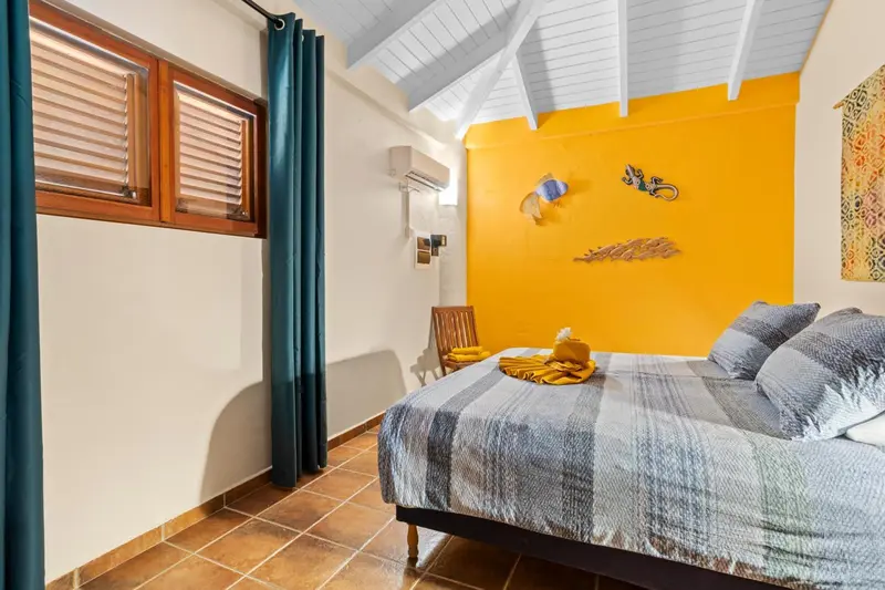 Une chambre lumineuse avec un lit recouvert d'une courtepointe grise et bleue.