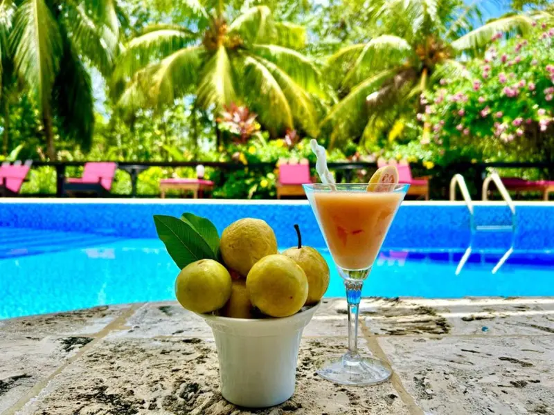 Un cocktail et des fruits tropicaux sont posés au bord d'une piscine turquoise.