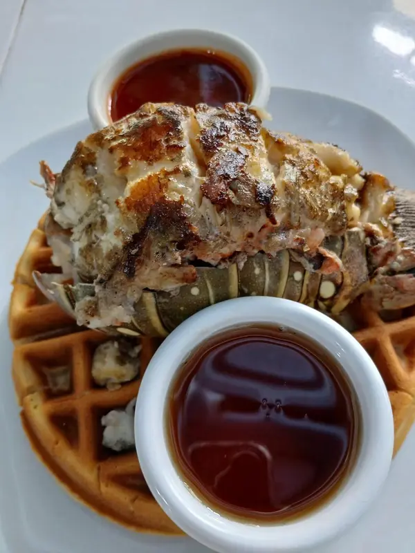 Un plat de homard grillé est servi sur une gaufre avec deux sauces.