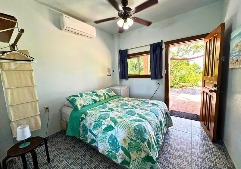 Une chambre lumineuse avec un lit recouvert d'une couette à motifs tropicaux et une porte ouverte sur l'extérieur.